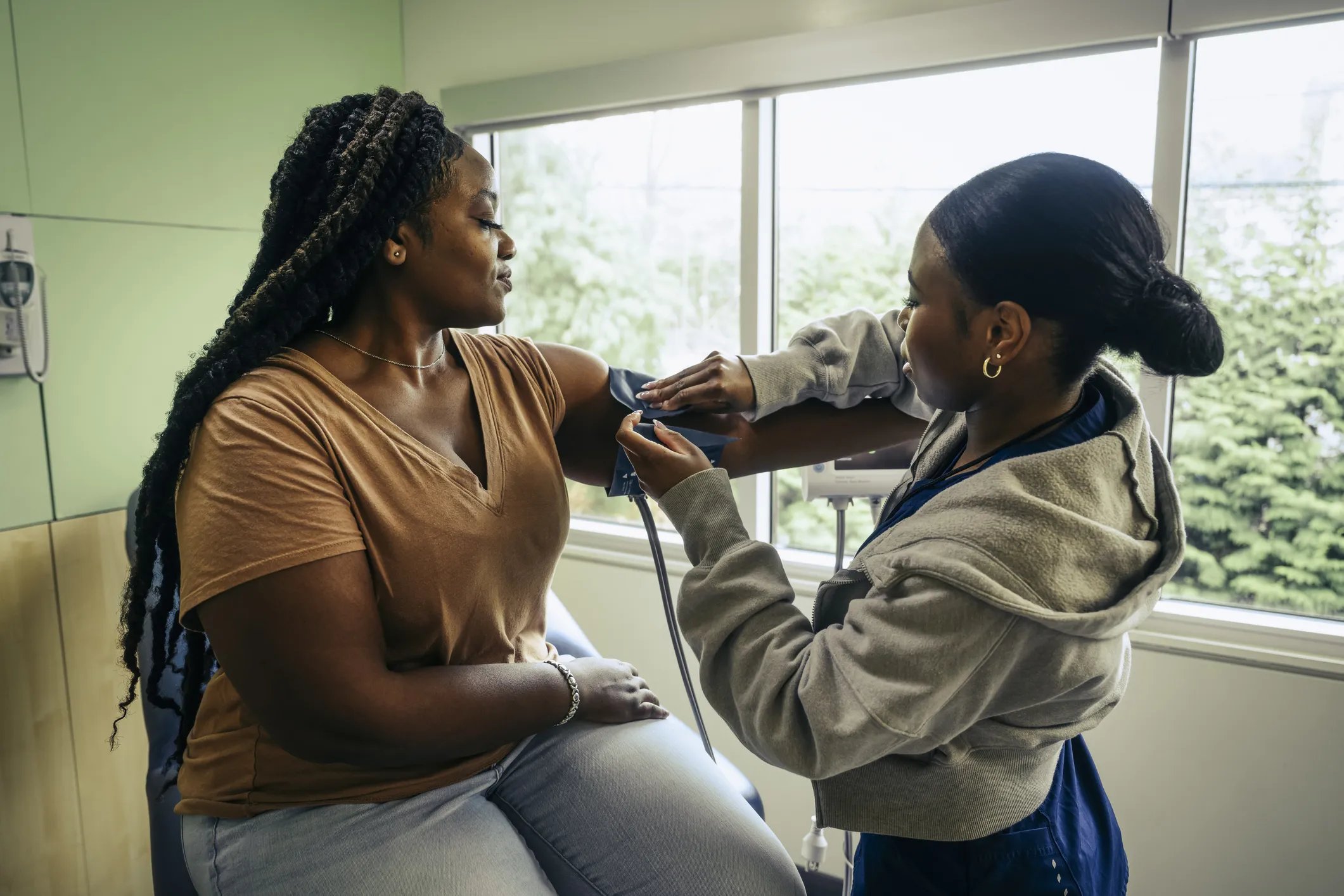 Young female nurse taking patient's blood pressure in examination room at doctor's office. She is being treated for hypertension.