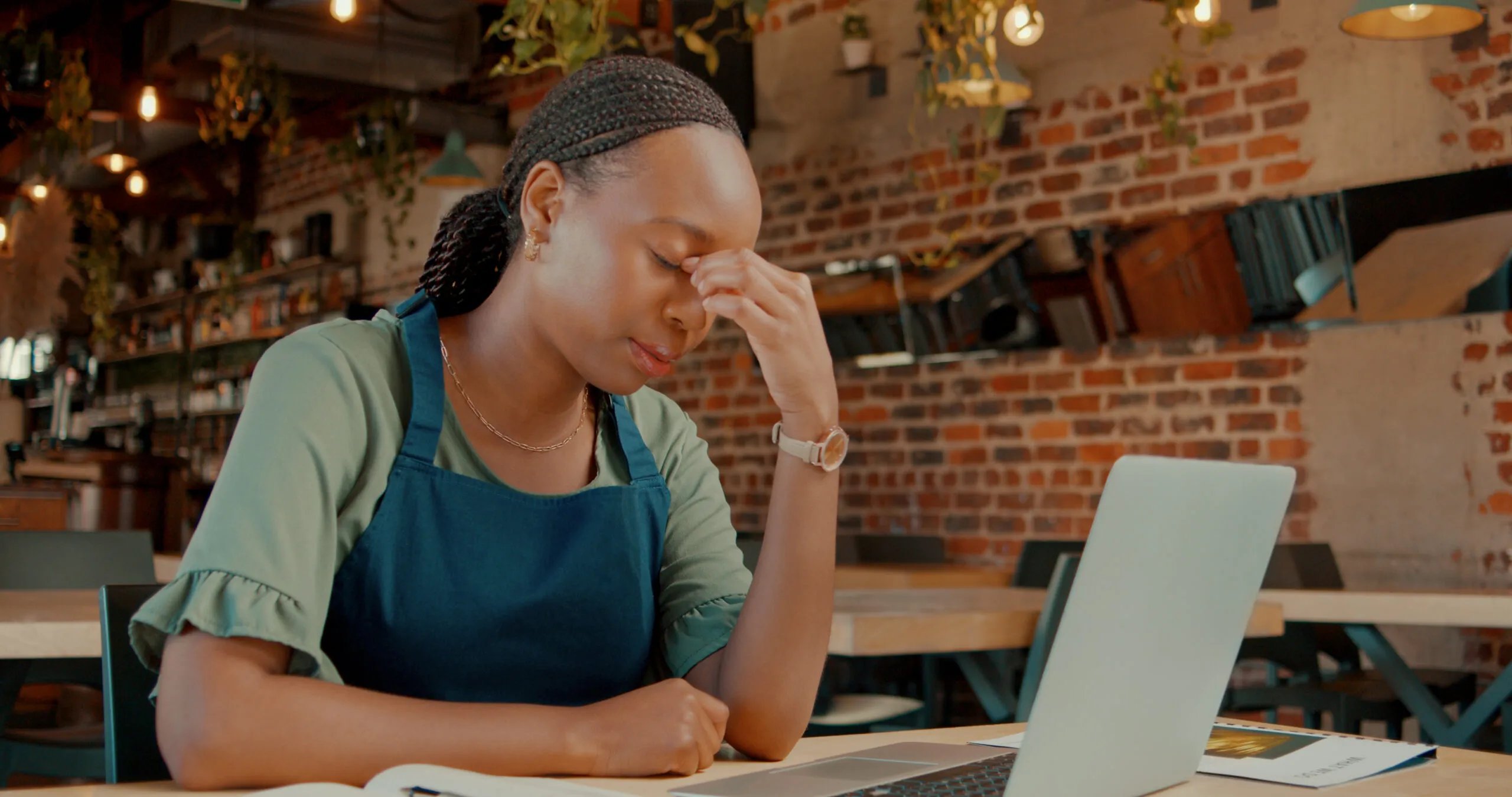 Owner, black woman and tired with laptop in restaurant for menu development or startup business planning for cafe. Girl, online and headache for long hours or financial pressure for profit sales.