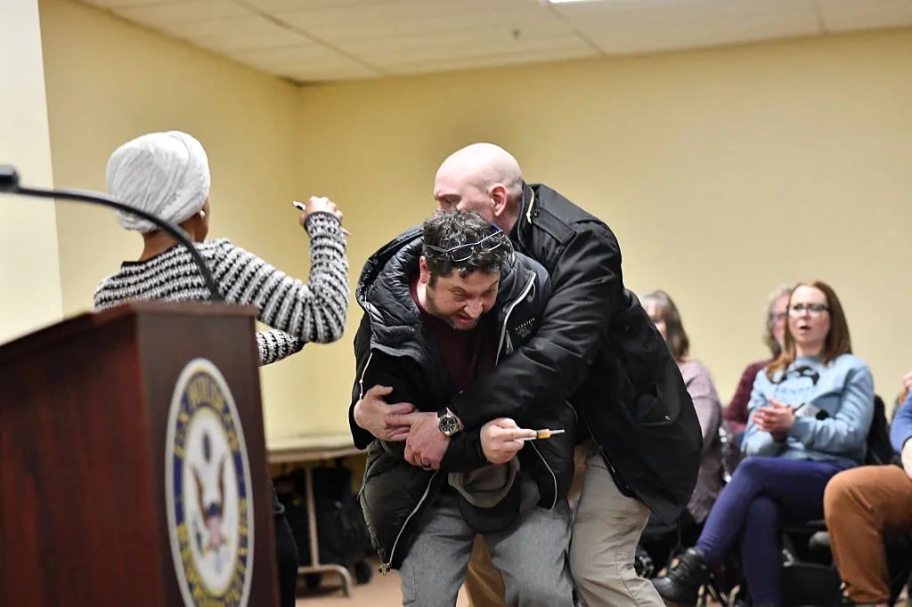 A man is tackled after spraying an unknown substance at US Representative Ilhan Omar (D-MN) (L) during a town hall she was hosting in Minneapolis, Minnesota, on January 27, 2026. US Democratic congresswoman Ilhan Omar was targeted during a speech late on January 27 by a man who sprayed an unidentified liquid at her from a syringe before being tackled by security guards, according to an AFP journalist at the scene. The man was led out of the premises as Omar, a frequent target of attacks by President Donald Trump, continued her speech saying "we will stay resilient in the face of whatever they might throw on us."