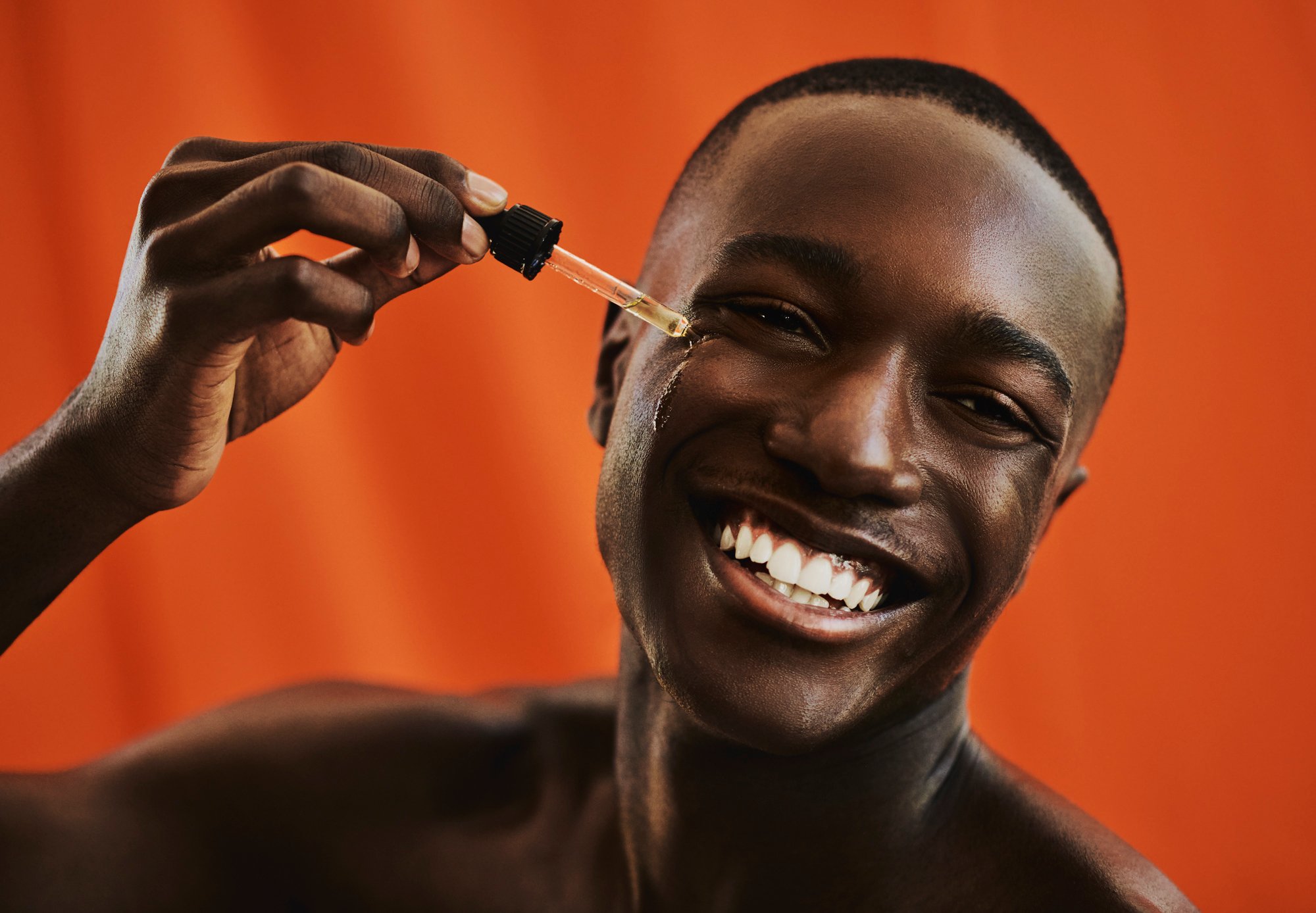 handsome young black man happily applies moisturising serum to his face, copy space, stock photo