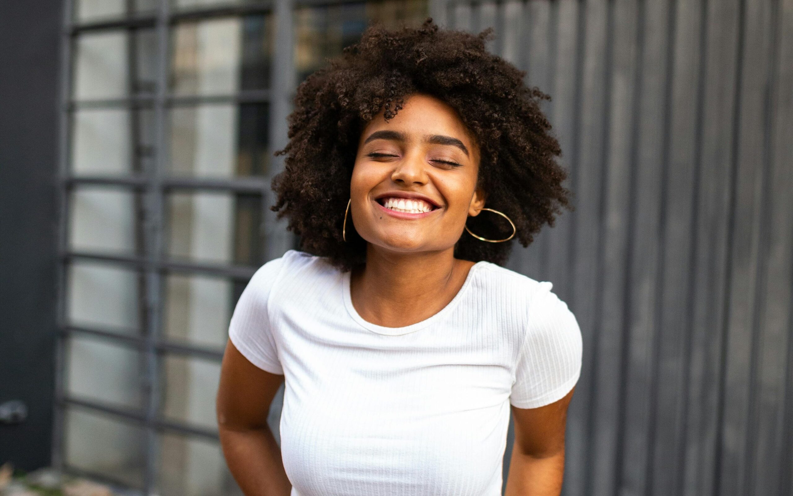 Woman with afro smiles at camera while wearing a white tee