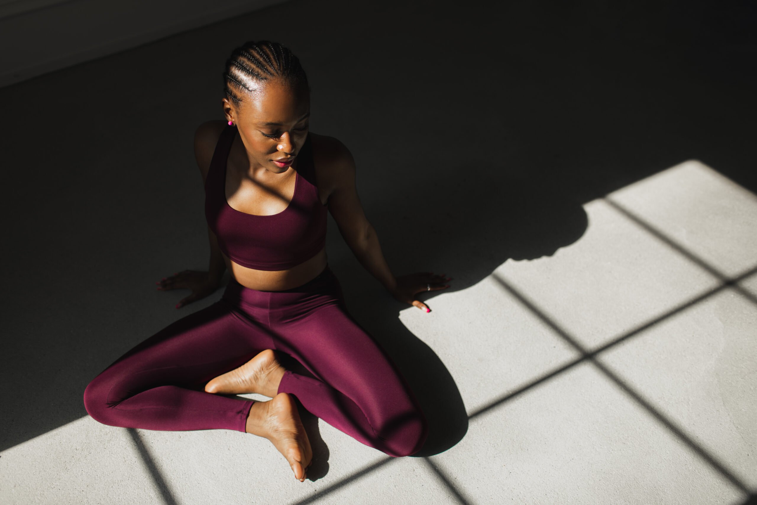 Fitness beautiful black woman with braided hair practicing yoga, stretching or doing exercising on white background. Fit millennial African American female being in great shape, leading active lifestyle. Contrast light.