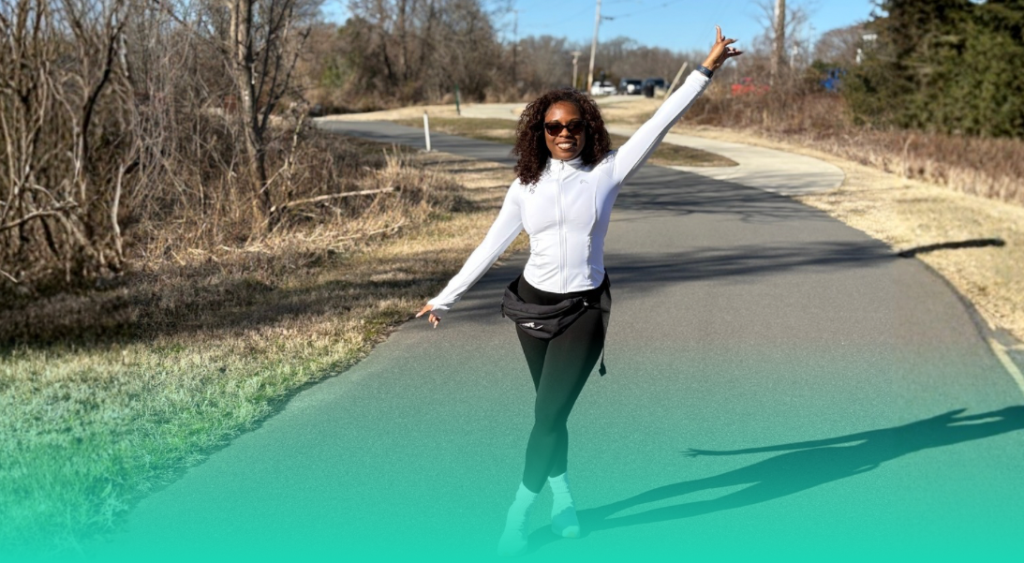 woman in a white jacket and black pants pausing for a picture while running on a trail