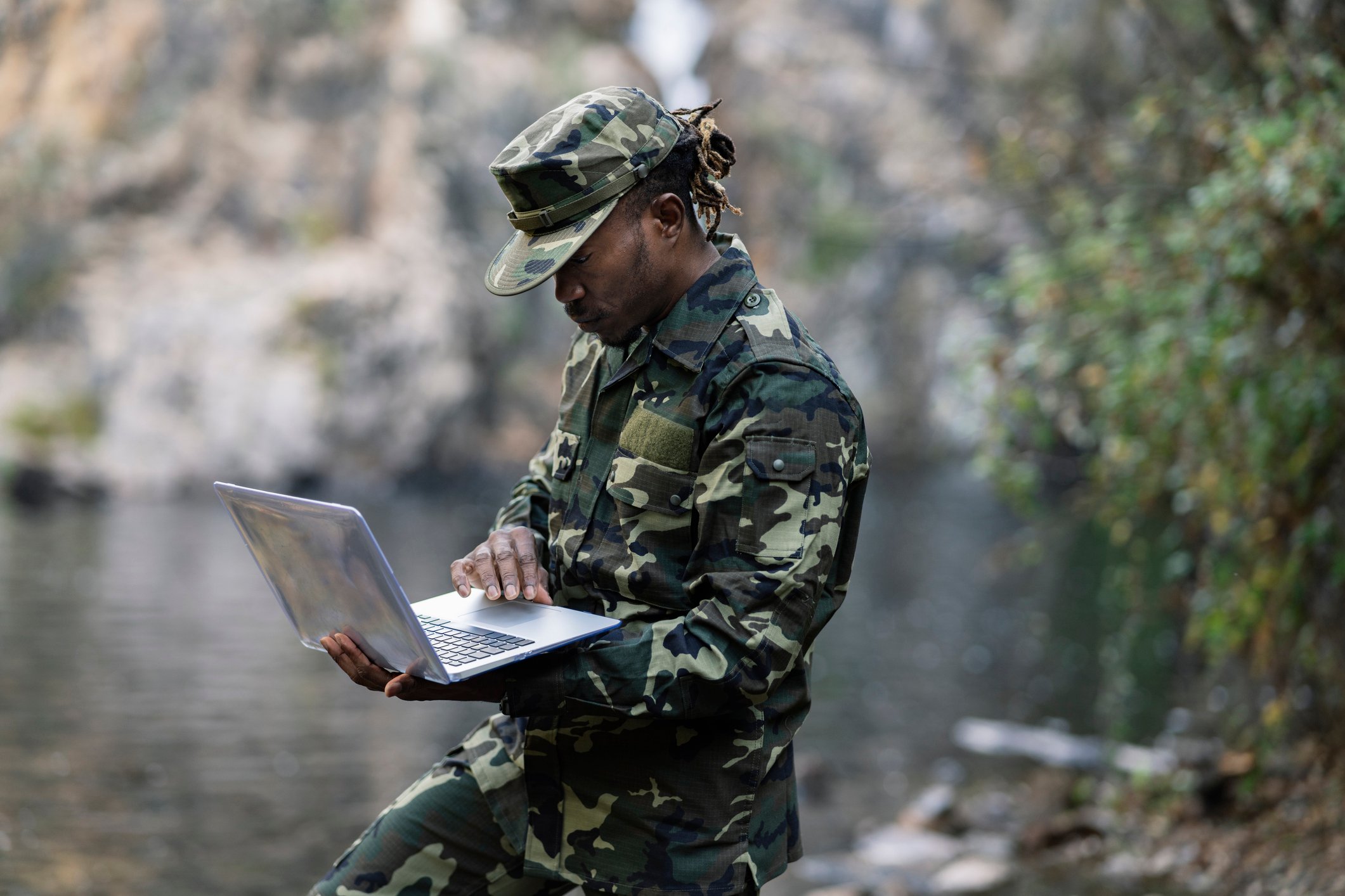 Black military man, with laptop, on duty in the jungle