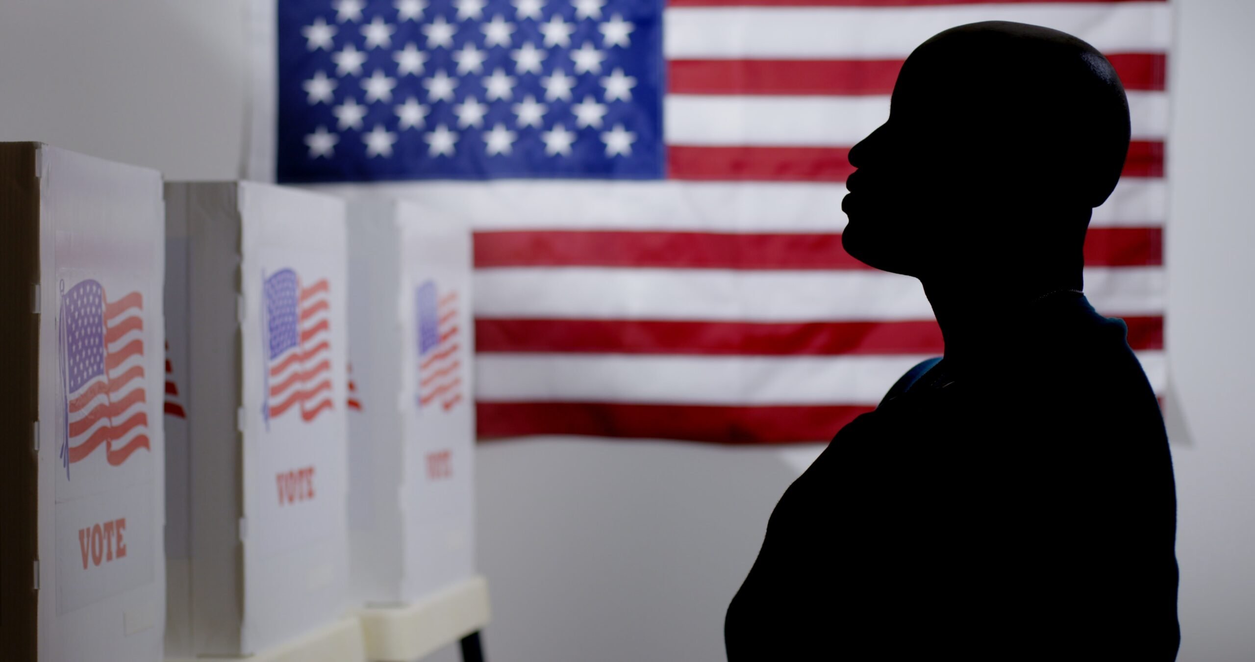 MS silhouetted African American man looking at voting booths, with hand over heart, US flag on wall behind