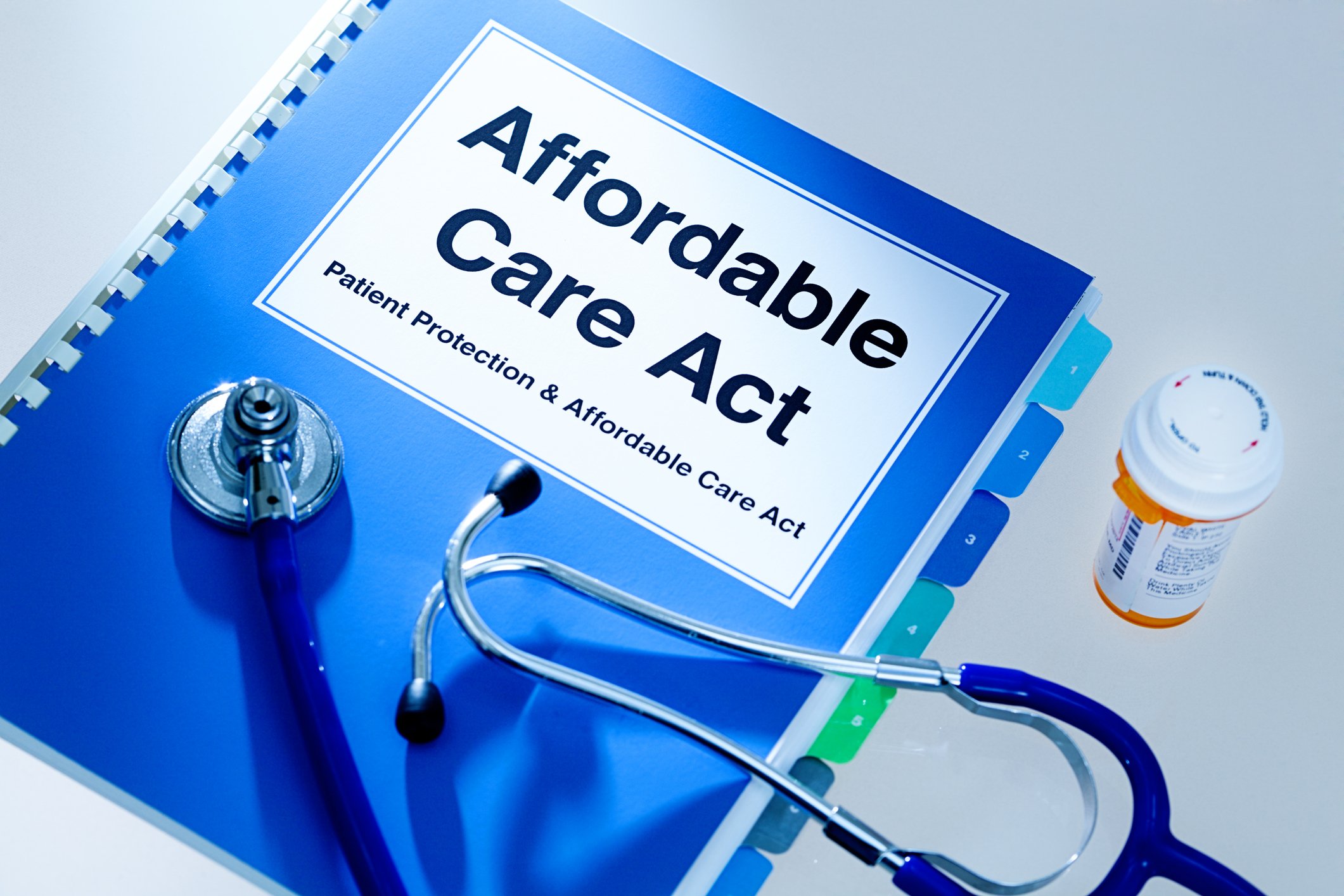 Still life of a manual handbook for the Patient Protection and Affordable Care Act with a stethoscope and prescription medication bottle. The manual is open to the title page, The open enrollment of the Affordable Care Act of the United States offers a health insurance program for all the U.S. citizens across the country.
