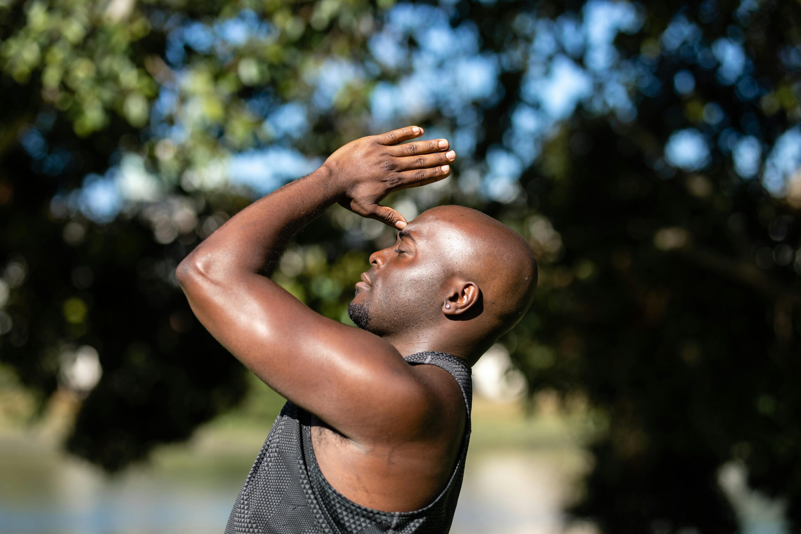 A Black bald man meditating and practicing baduanjin outdoors with a blurred natural background.