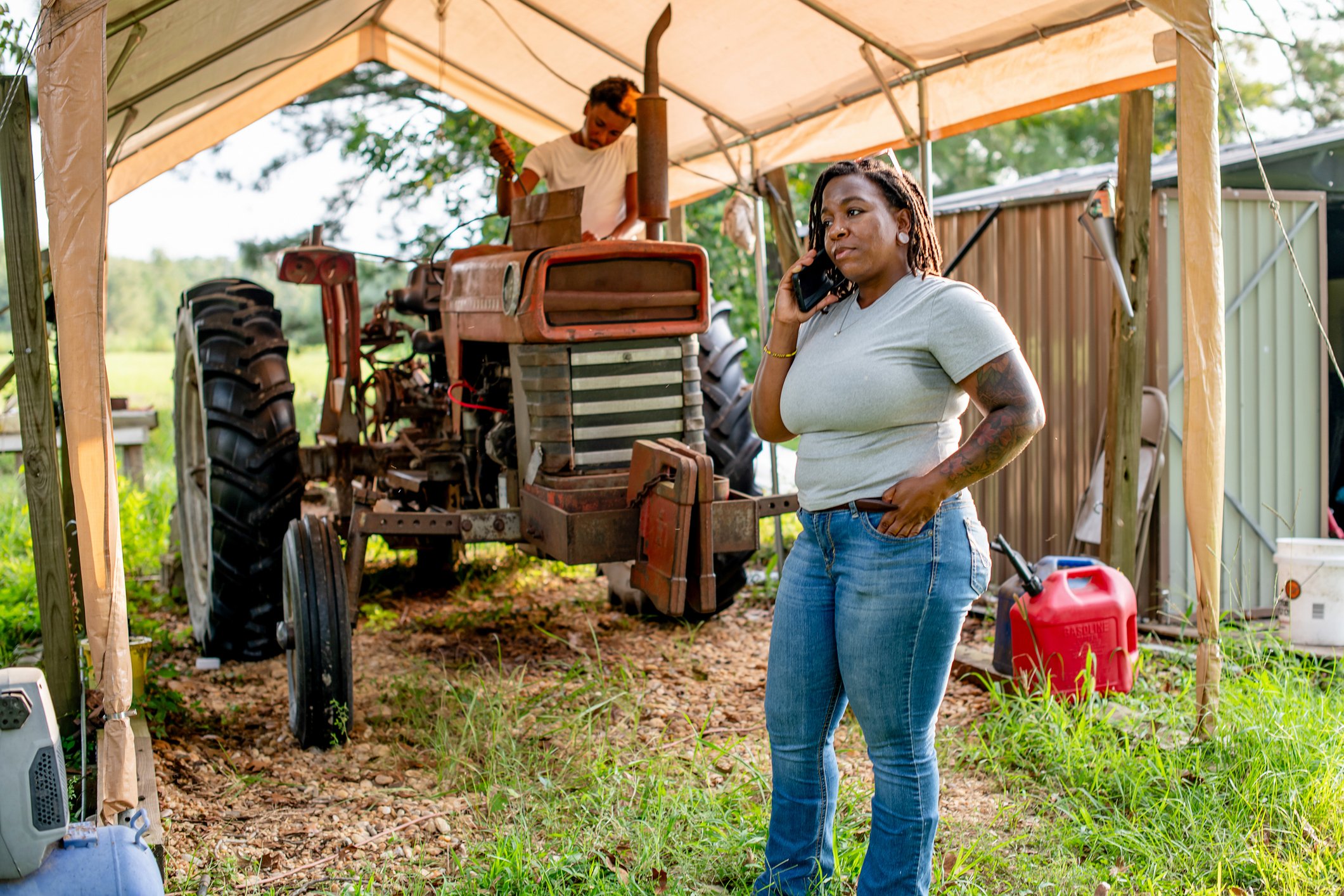 Female farmer on phone with son in background on tractor