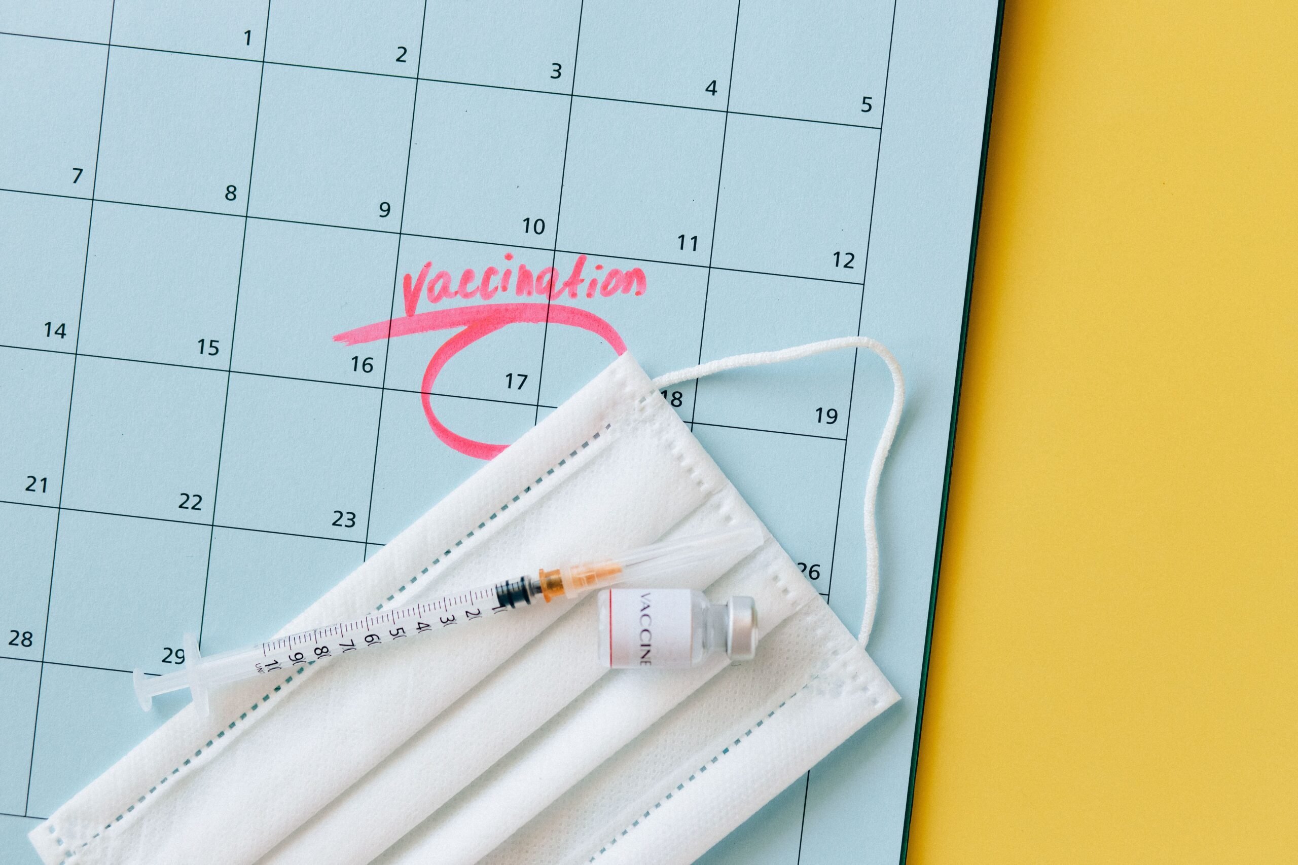 Close-up of a calendar marked for vaccination, with a syringe and face mask highlighting healthcare theme.