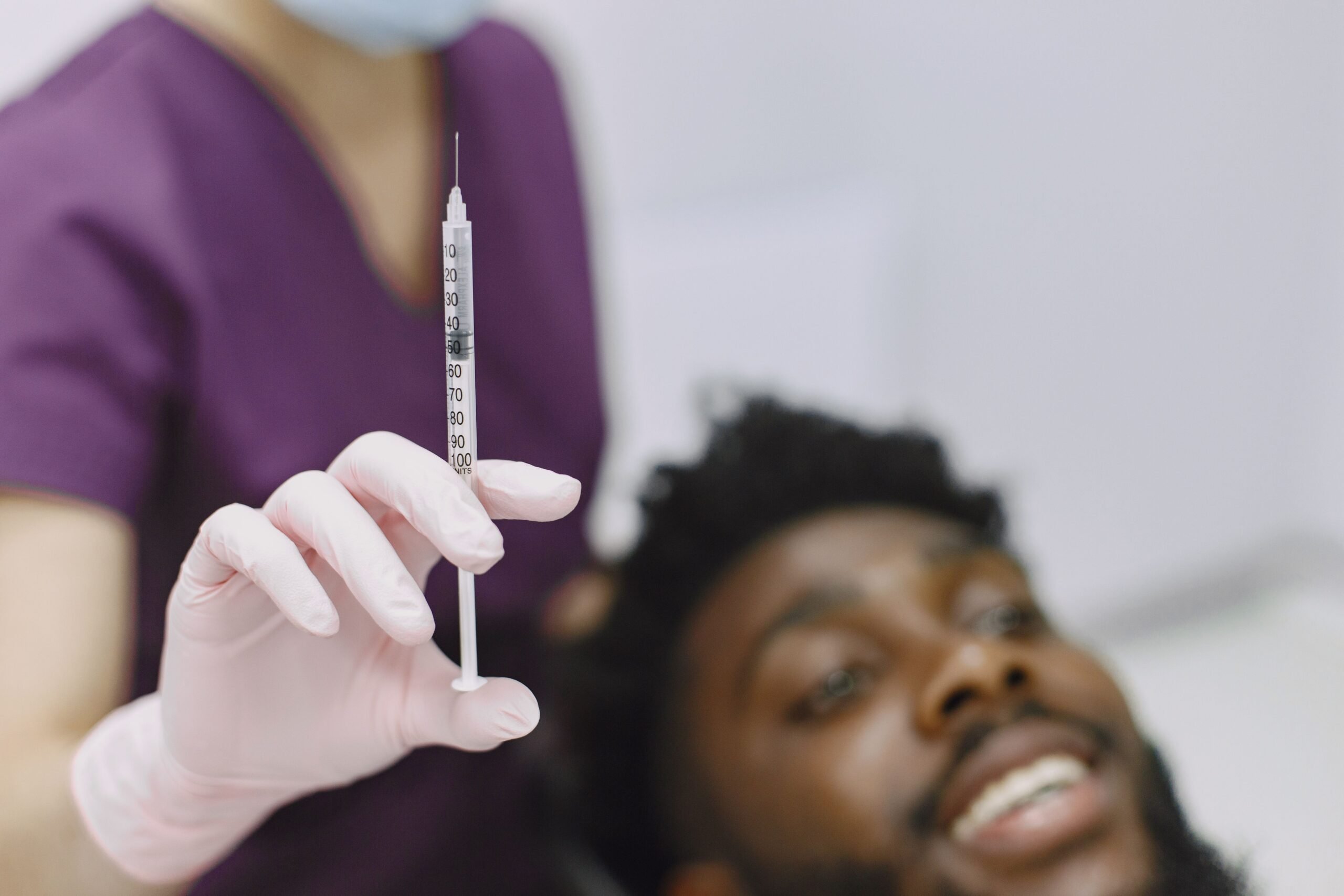 Close-up of a healthcare worker preparing a syringe for an injection, with a patient in the background.