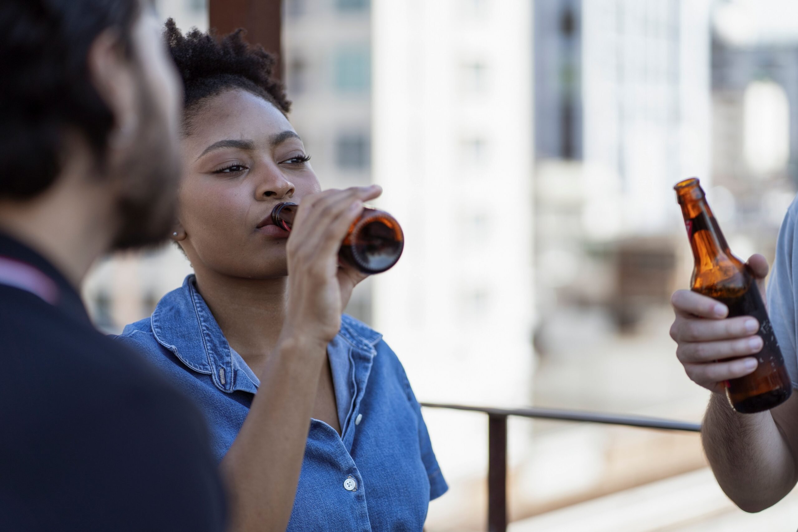 Three people enjoying a casual drink outdoors, sharing beers under daylight.
