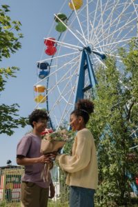 Young man giving a bouquet of flowers to a young woman in front of a ferris wheel.