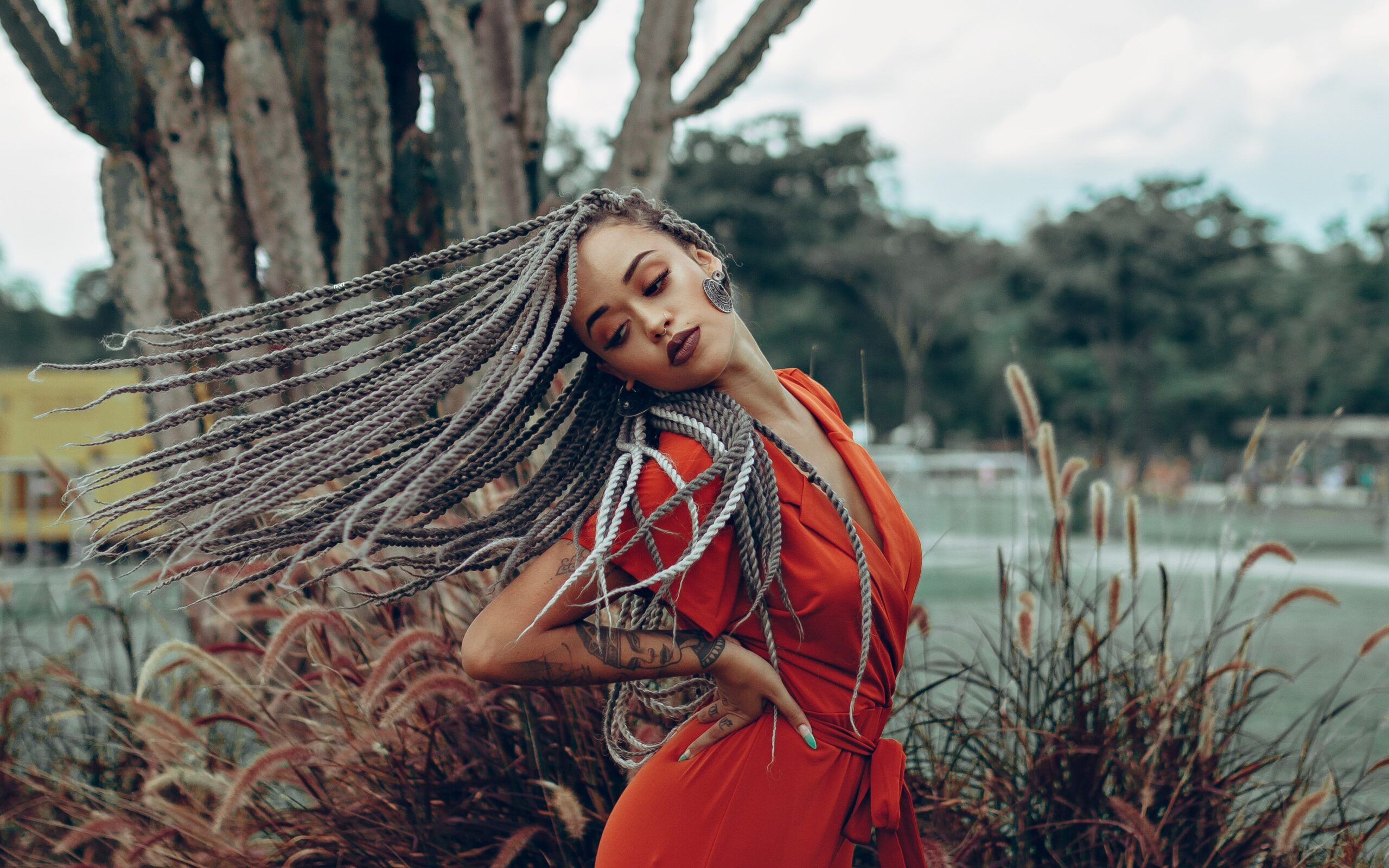 Black woman posing in red jumpsuit with braids outside