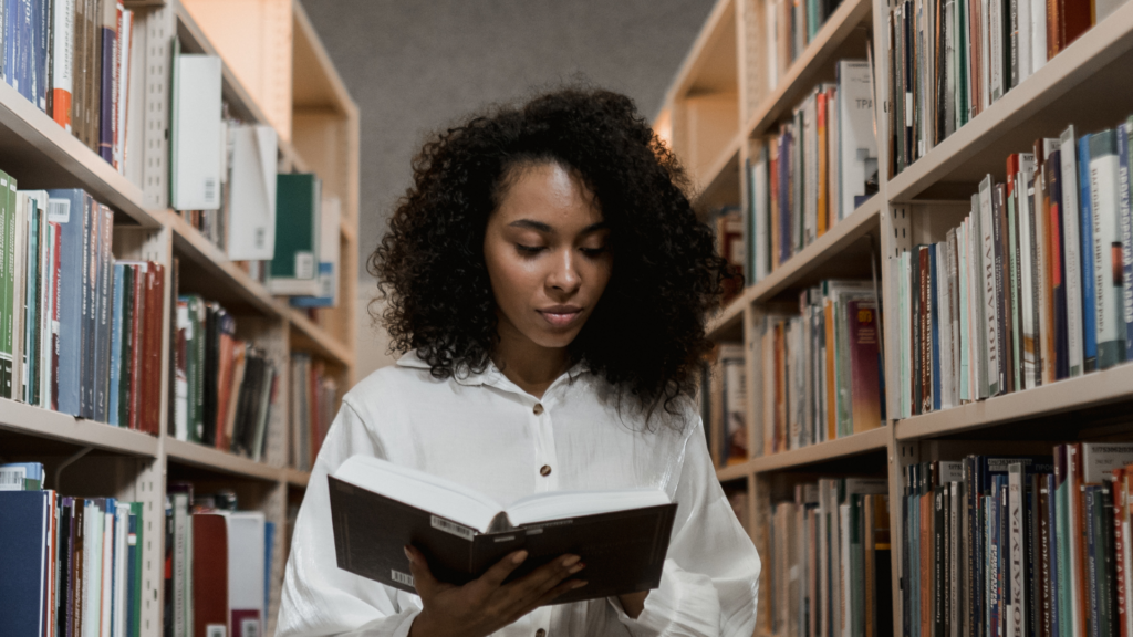 A Woman Reading a Book at the Library in between two rows of books