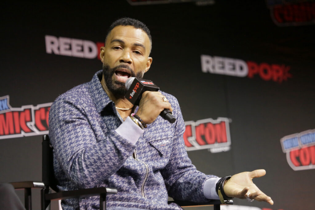 Omari Hardwick holding a mic and speaking while on a panel for a film event