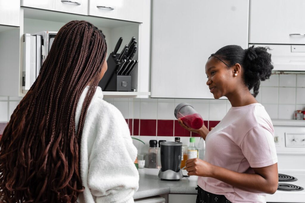 Two ladies talk in kitchen, and one is holding ingredients in a blender