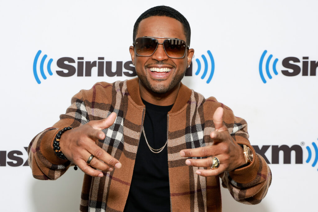 Larenz Tate points fingers at camera while wearing a brown, black and tan plaid shirt during his visit to SiriusXM Studios on May 24, 2023 in New York City. 