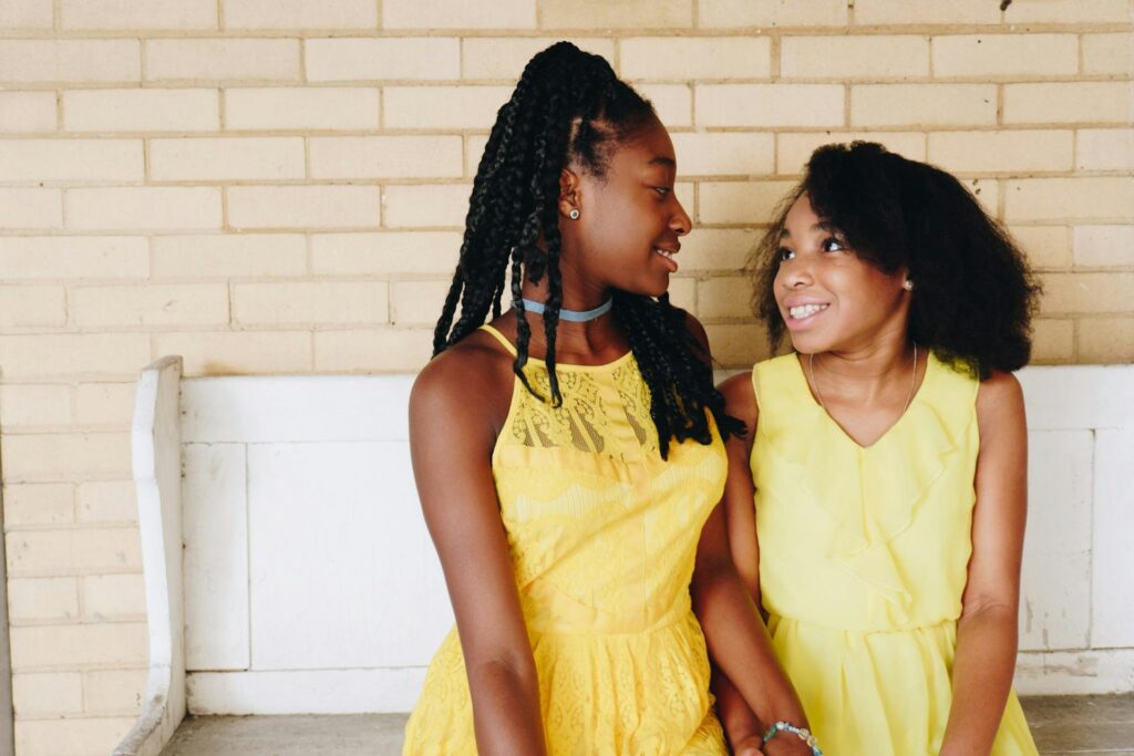 Two girls wearing yellow sit closely next to each other on a bench