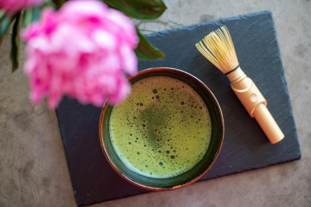 A close-up image of a glass of matcha next to a pink flower. strawberry-matcha